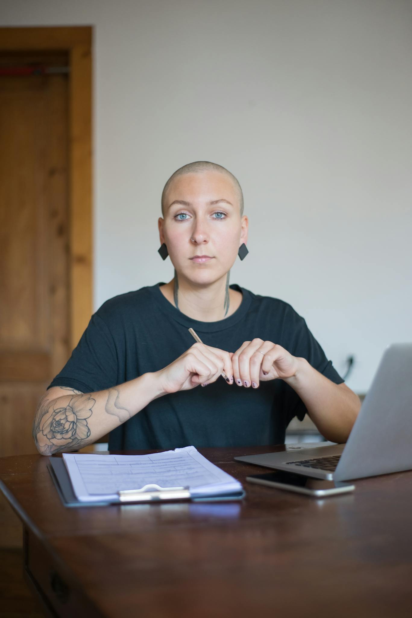 A bald woman working from home, focusing on a laptop and documents, representing health and empowerment.