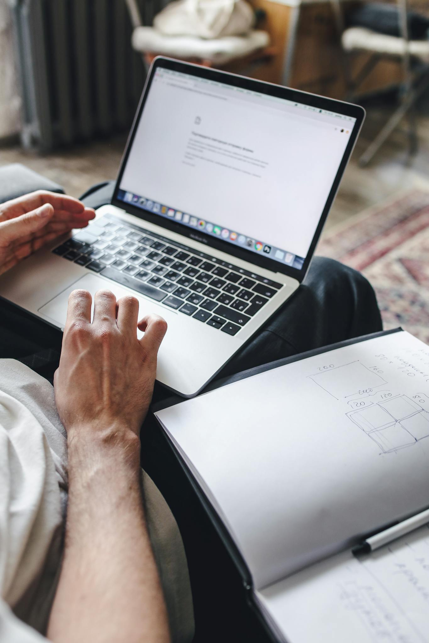 Close-up of a person using a laptop with a notebook open beside it, focusing on hands and typing.